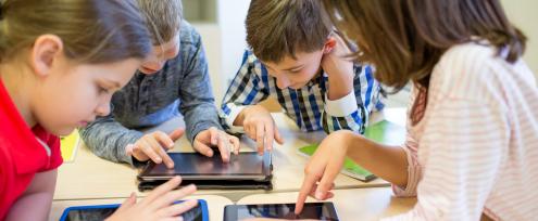 4 børn rundt om et bord med ipads